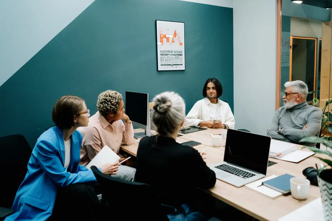 A team meeting around a boardroom table with laptops, notebooks and coffee cups